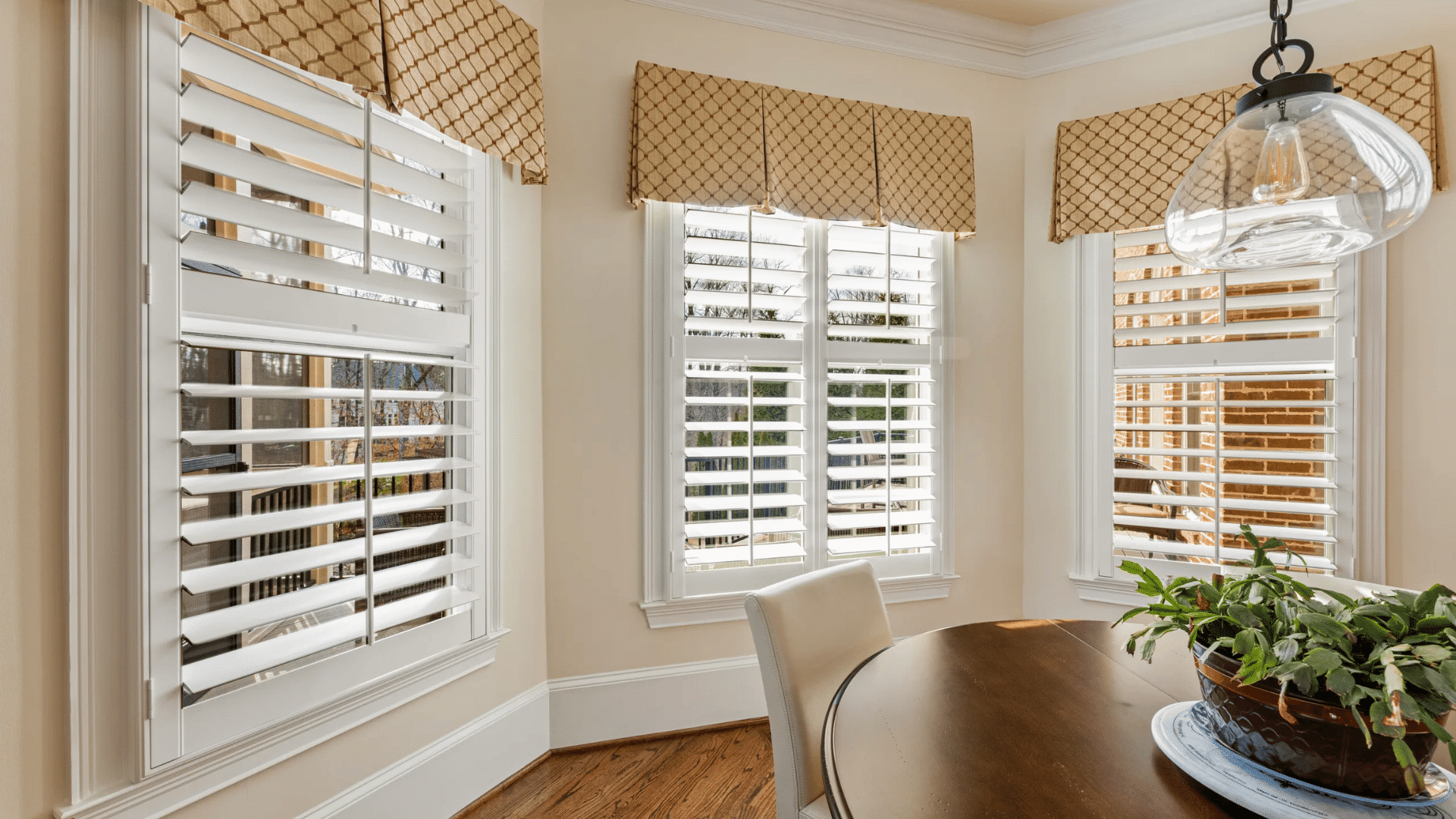 white plantation shutters with patterned valances in a bright dining room with wood table and large windows
