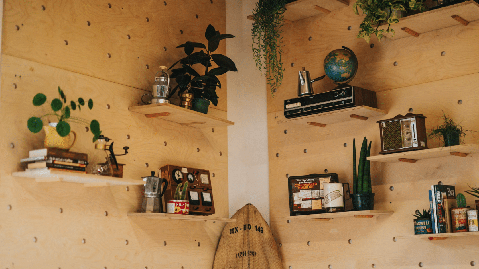 wooden pegboard wall with floating shelves displaying plants books vintage decor and coffee accessories in a cozy room interior