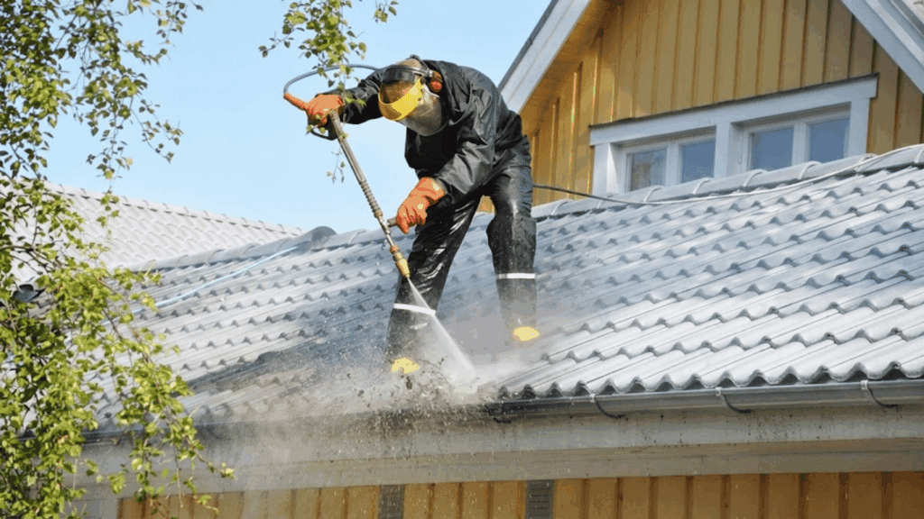 a worker wearing protective gear pressure washing a tiled house roof while standing safely on the rooftop in daylight