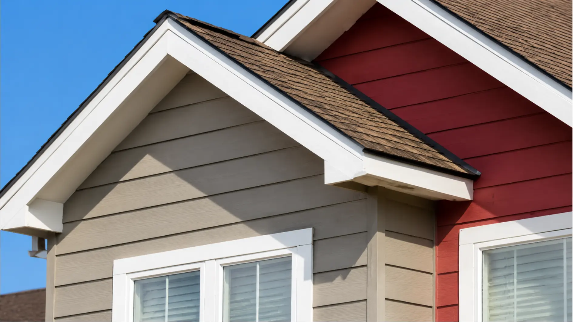 Close-up view of abbreviated eaves on a gable roof with white trim, dark shingles, and contrasting house siding.
