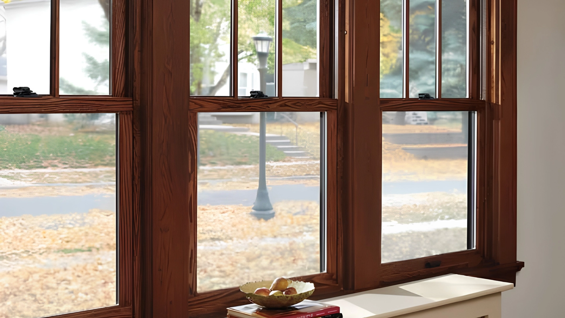 Rich dark wood double-hung window frame showing an outdoor autumn view near a windowsill.
