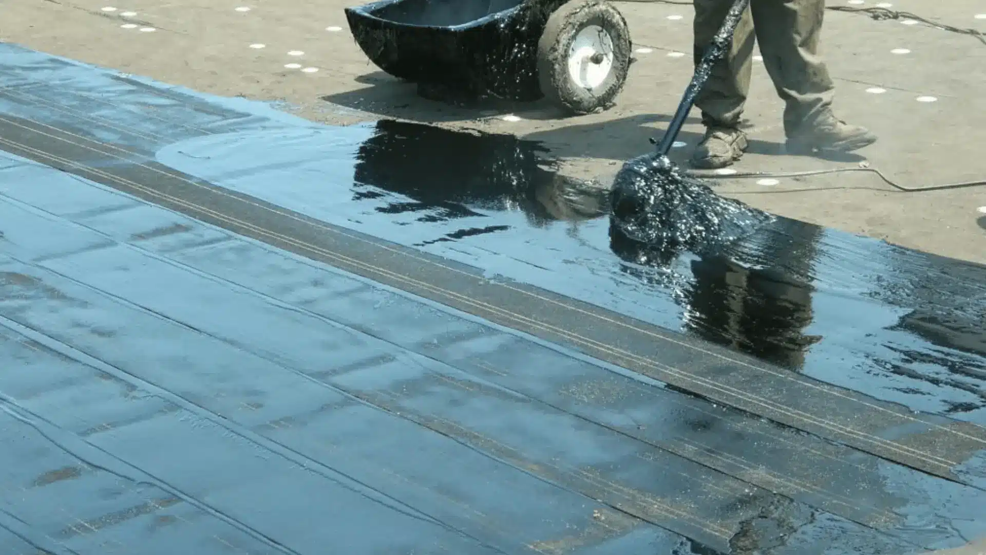 Roofer applying black waterproof coating to a flat roof surface