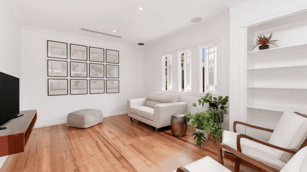 bright modern living room with white sofa wooden floors framed wall art large windows and indoor plants