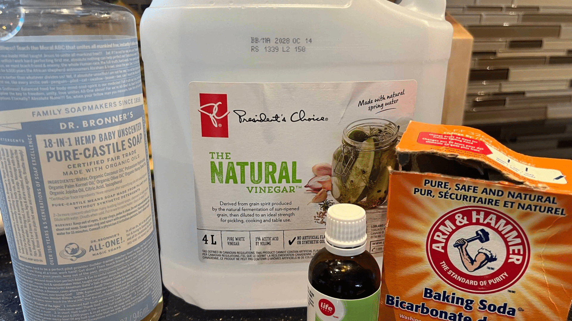 diy toilet cleaner ingredients including castile soap white vinegar baking soda and tea tree oil arranged on a kitchen countertop for homemade cleaning solution