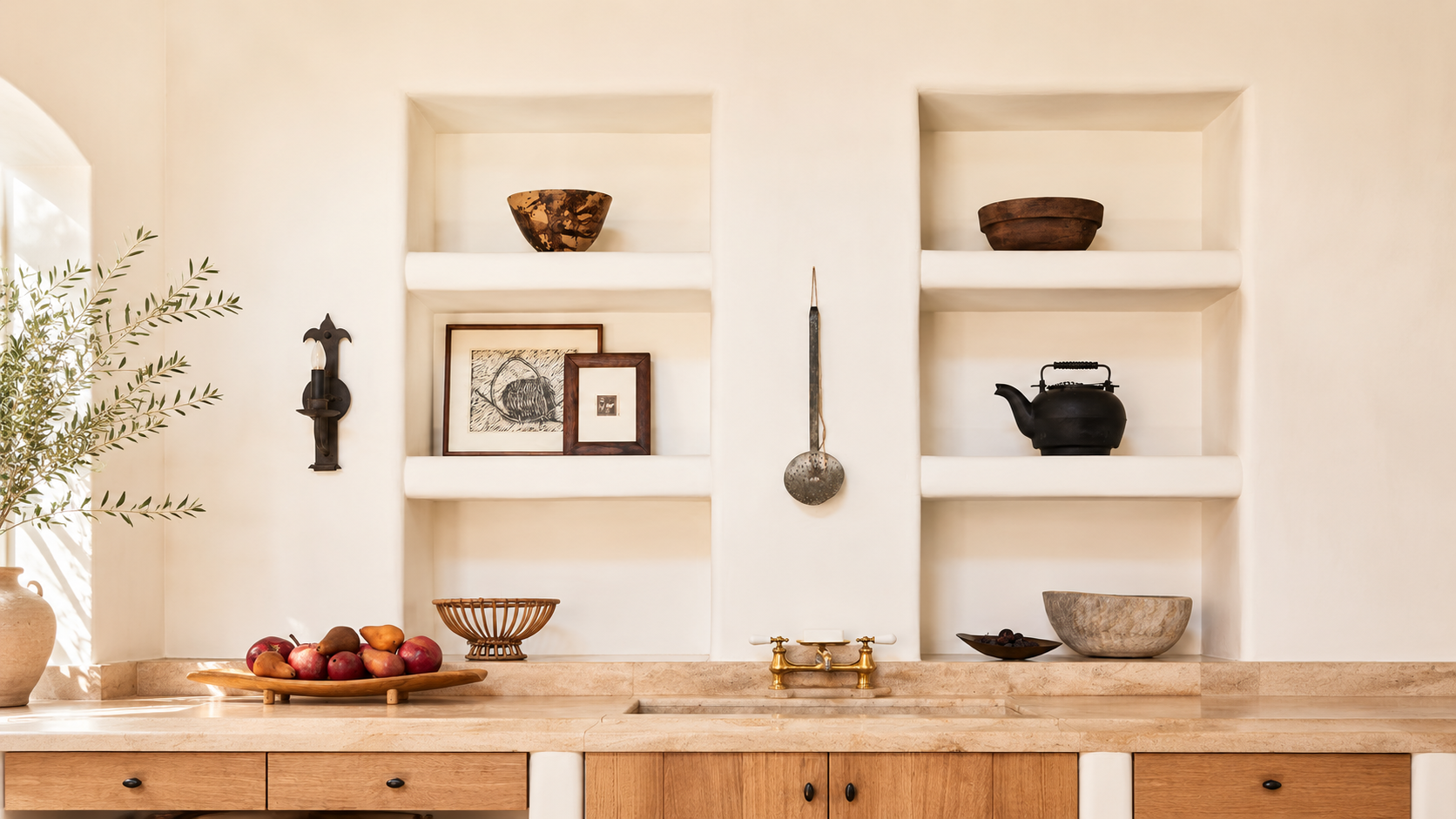 Built-in kitchen shelves with rustic decor, framed art, bowls, and a teapot above a warm stone countertop.