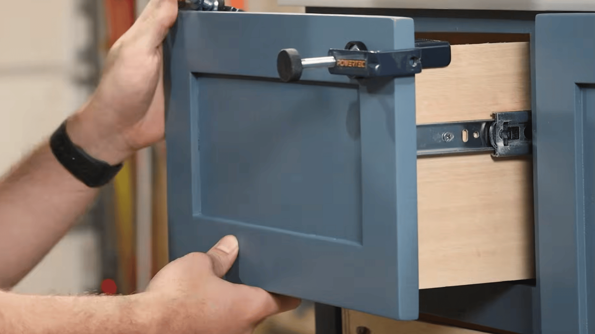 Installing drawer fronts and hardware on a blue painted vanity cabinet during final assembly.