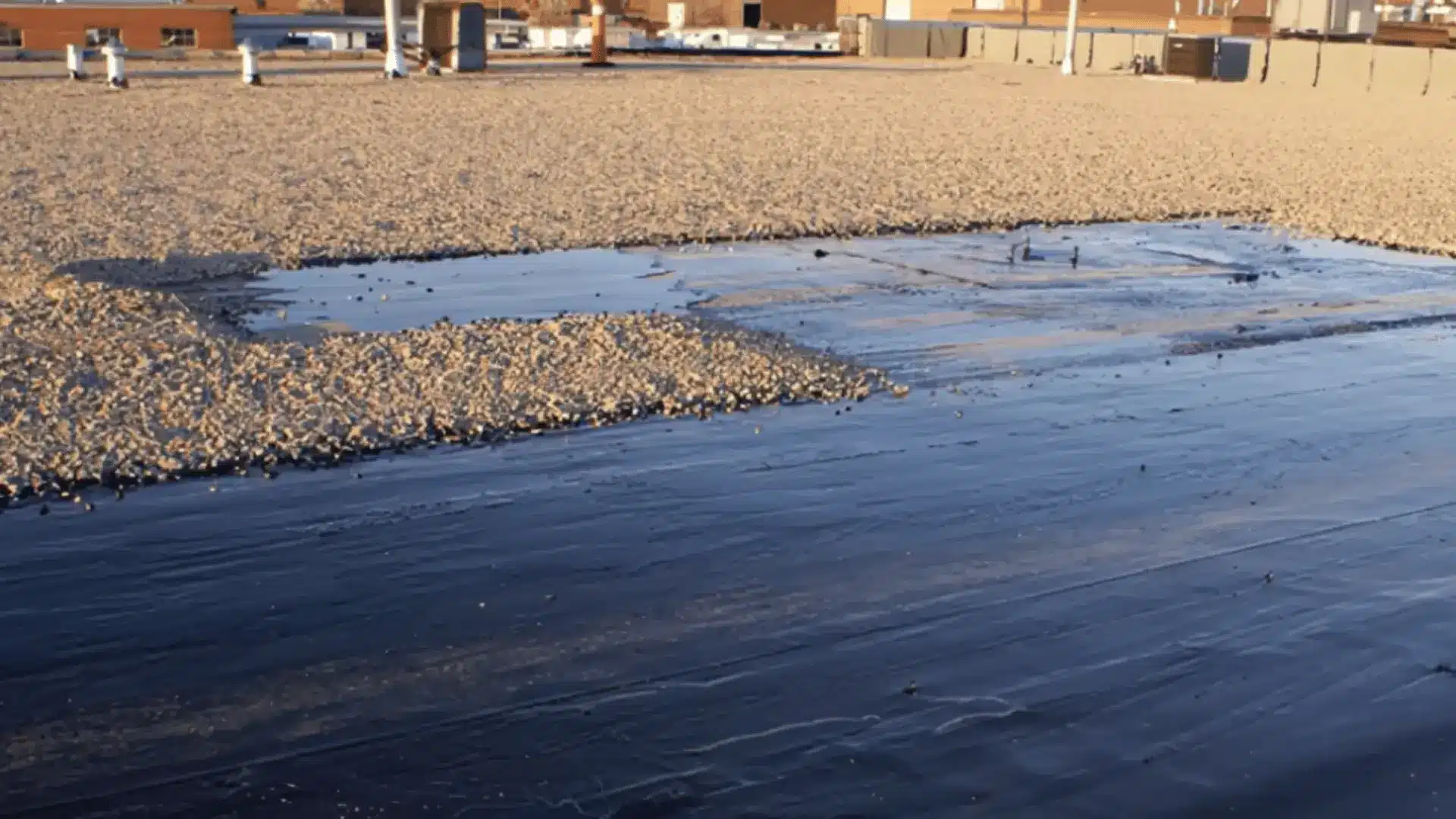 Flat gravel roof with a dark waterproof membrane section and rooftop fixtures