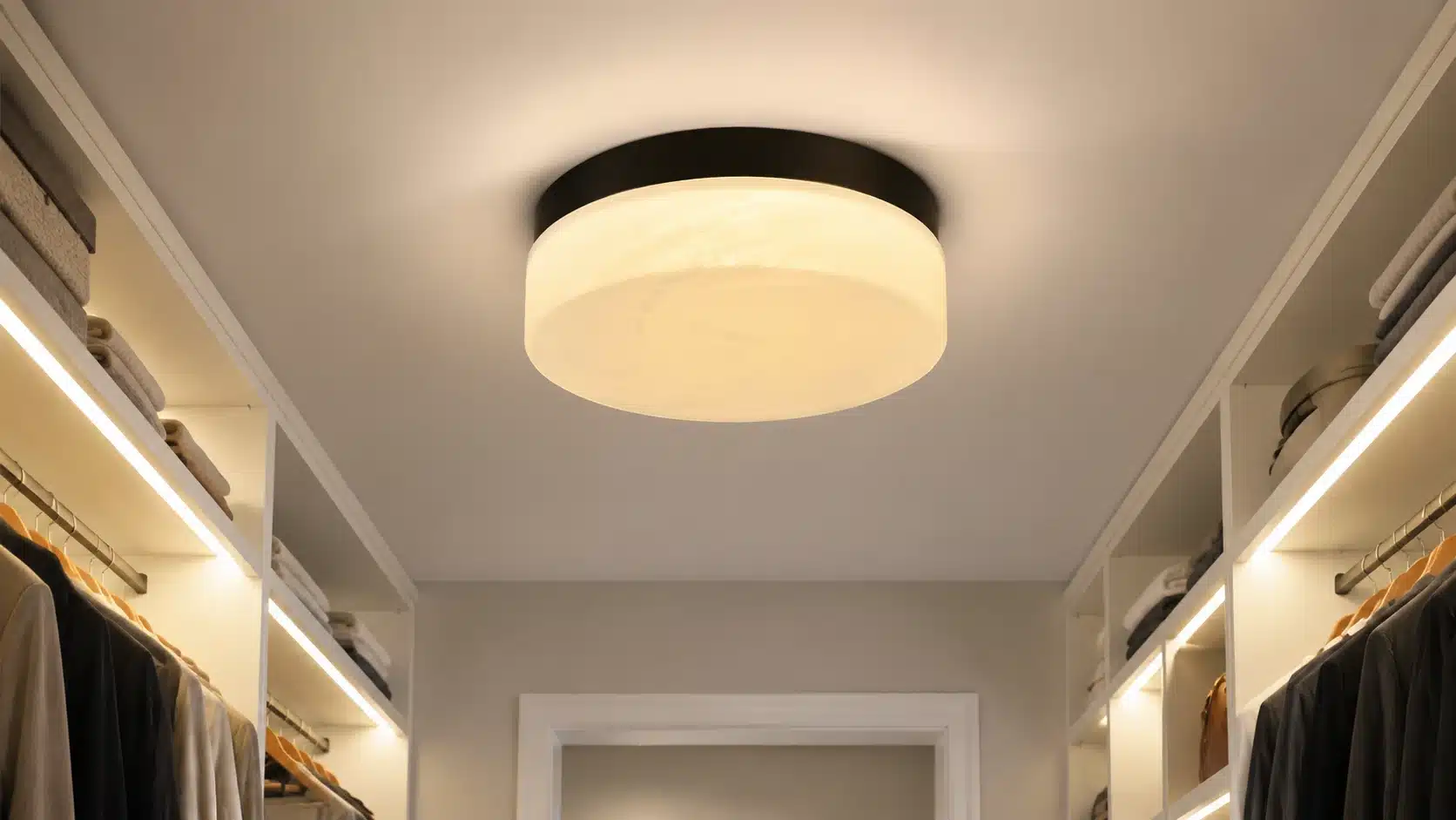 Modern walk-in closet with a large ceiling light as the focal point, creating soft ambient illumination with built-in shelf lighting.