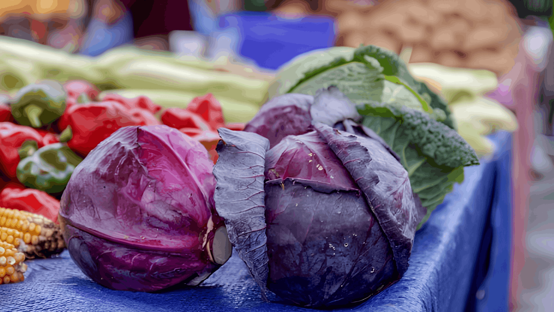 fresh red and green cabbages displayed on a market stall with colorful vegetables in the background ready for sale and cooking
