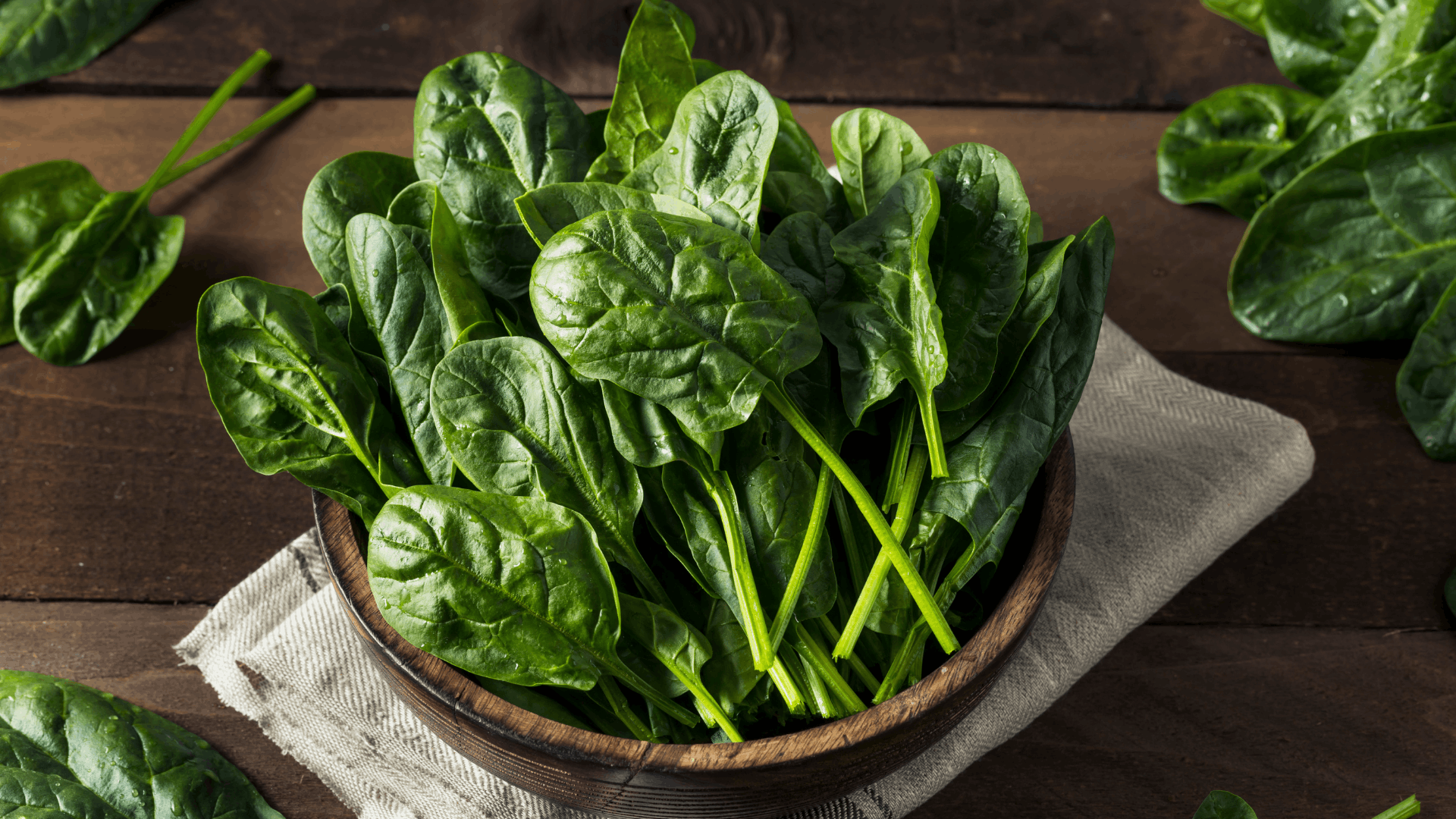 fresh spinach leaves in a wooden bowl showing nutritious greens used as eggplant companion plants