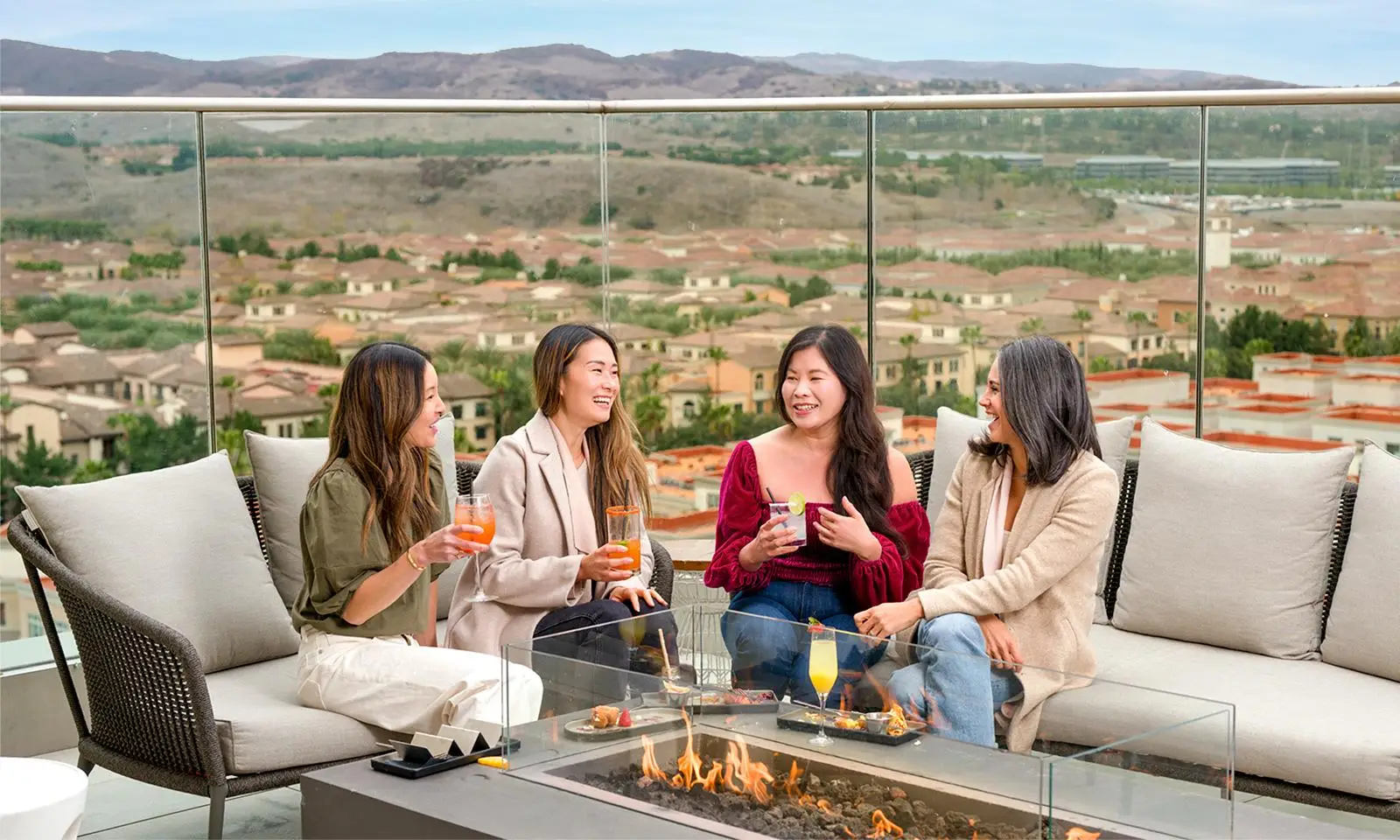 Four women enjoying drinks around a fire pit on a rooftop patio