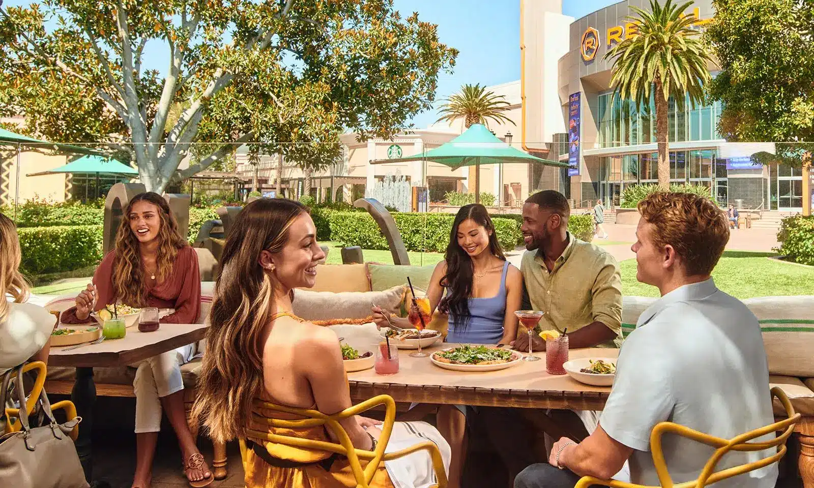 Group of friends dining outdoors at a sunny restaurant patio with salad and cocktails