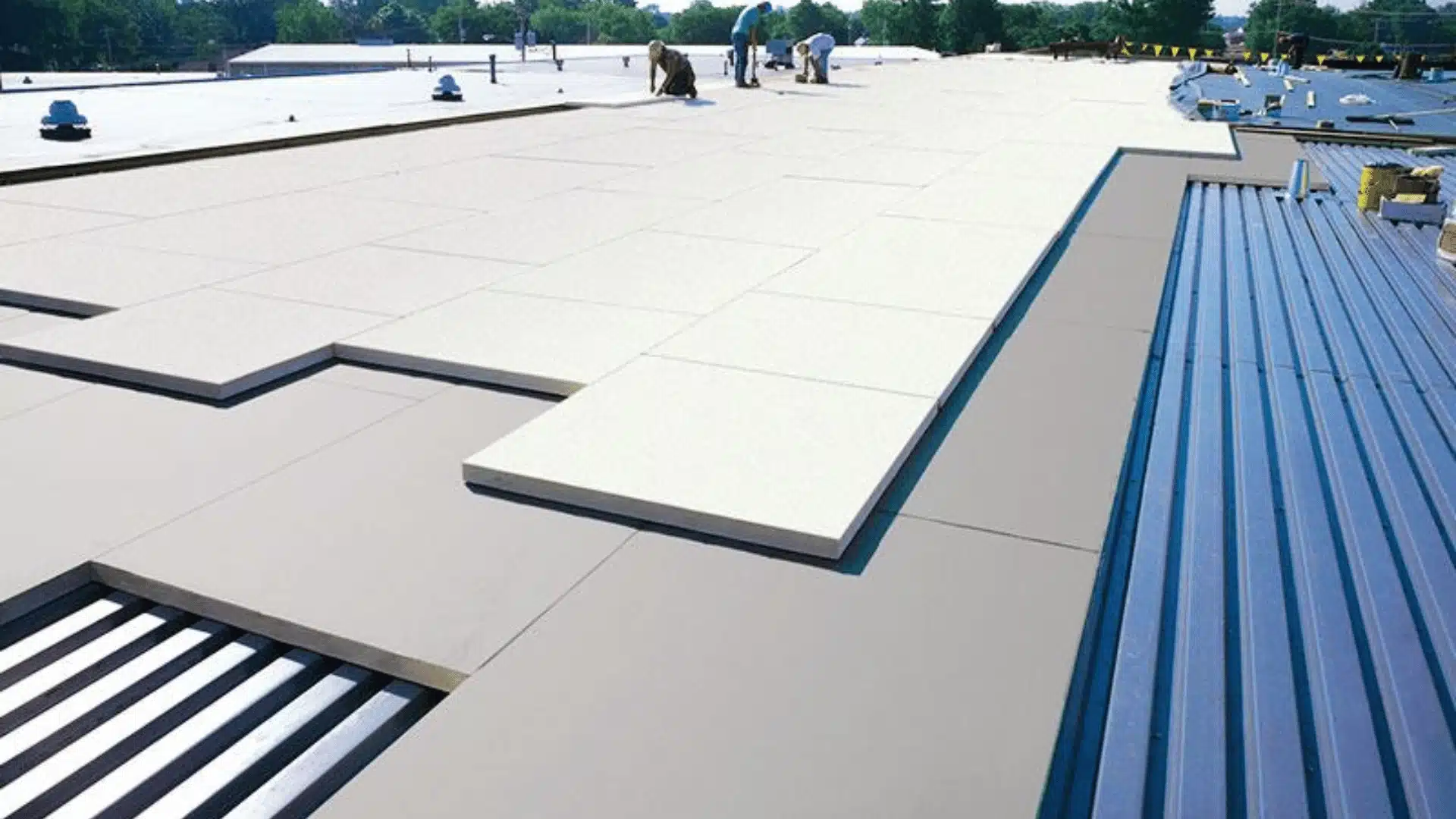 Flat roof installation with insulation boards, membrane layers, and metal roofing sections under construction.
