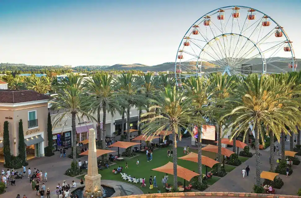 Irvine’s Liveliest Apartment Communities: Where to Rent Near Top Dining, Entertainment & Social Life Ferris wheel towering over outdoor shopping plaza with palm trees and people strolling