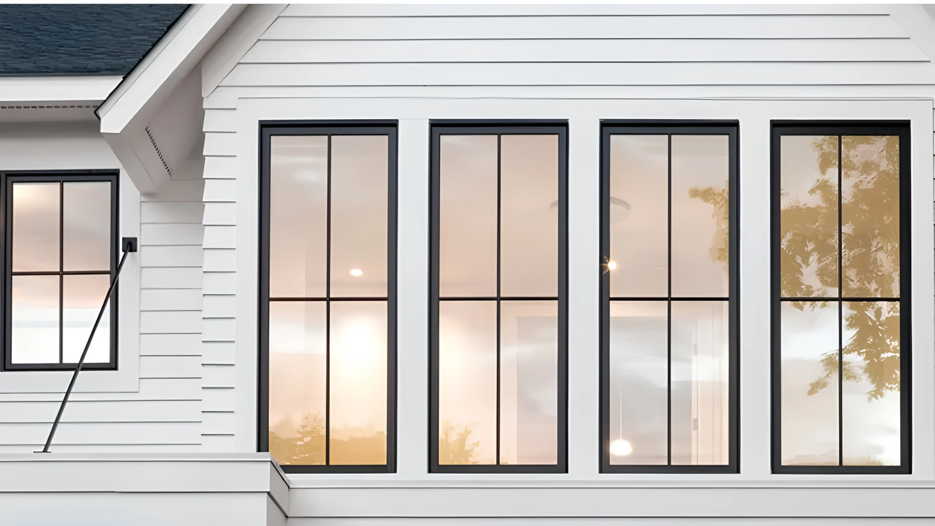 Four tall black-framed glass windows with interior lighting set into white siding exterior.