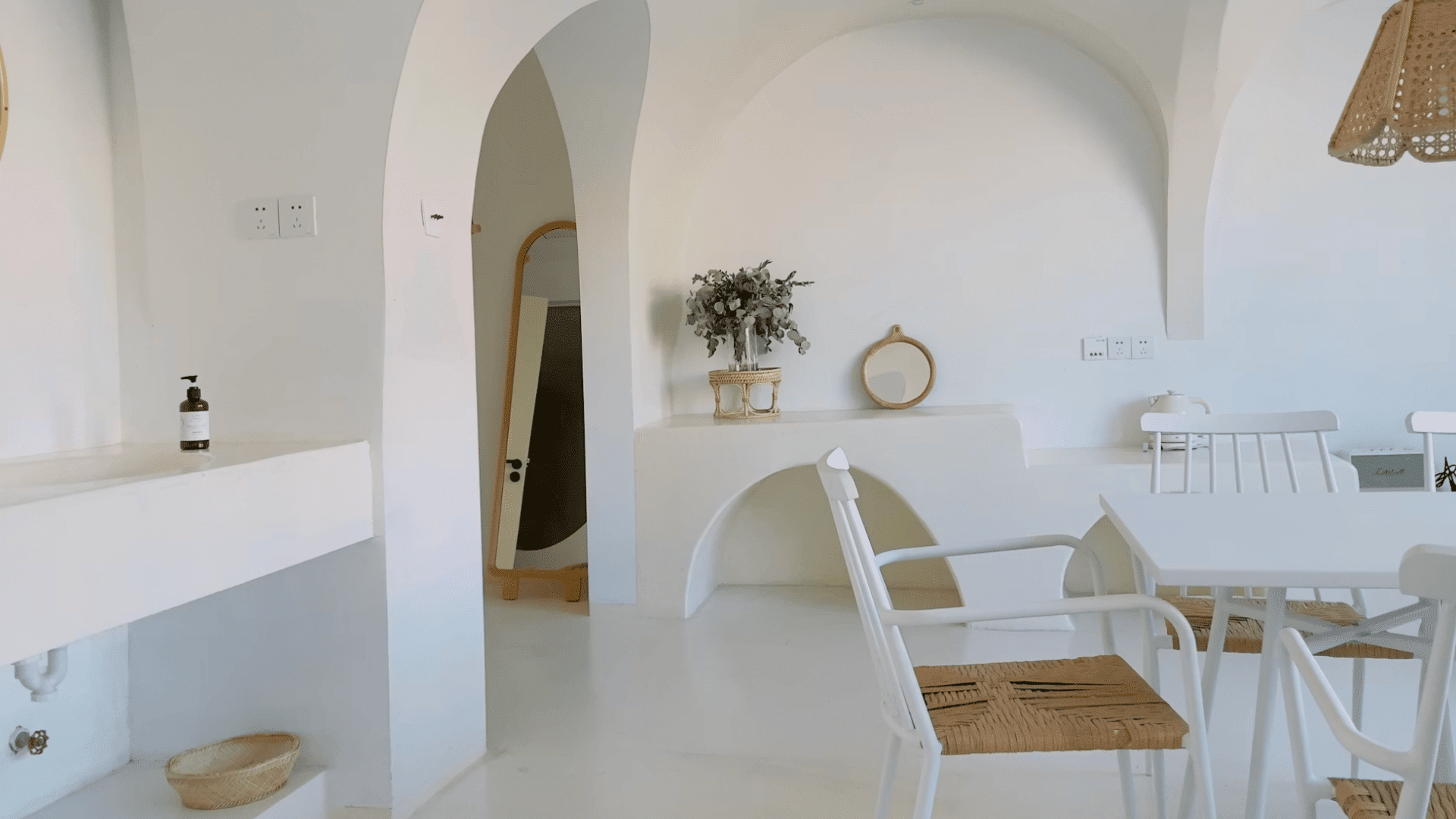 minimalist white interior room with arched doorways white chairs wicker accents plants and mirror on ledge