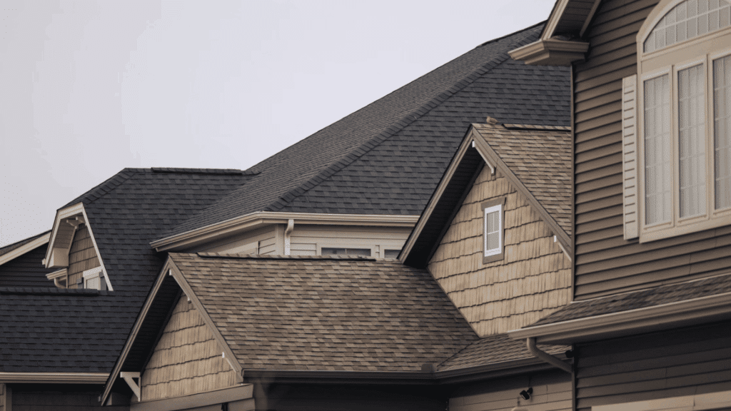 How Long Does a Roof Last: Average Lifespan by Material modern suburban homes with clean asphalt shingle roofs and multiple gables under a clear overcast sky