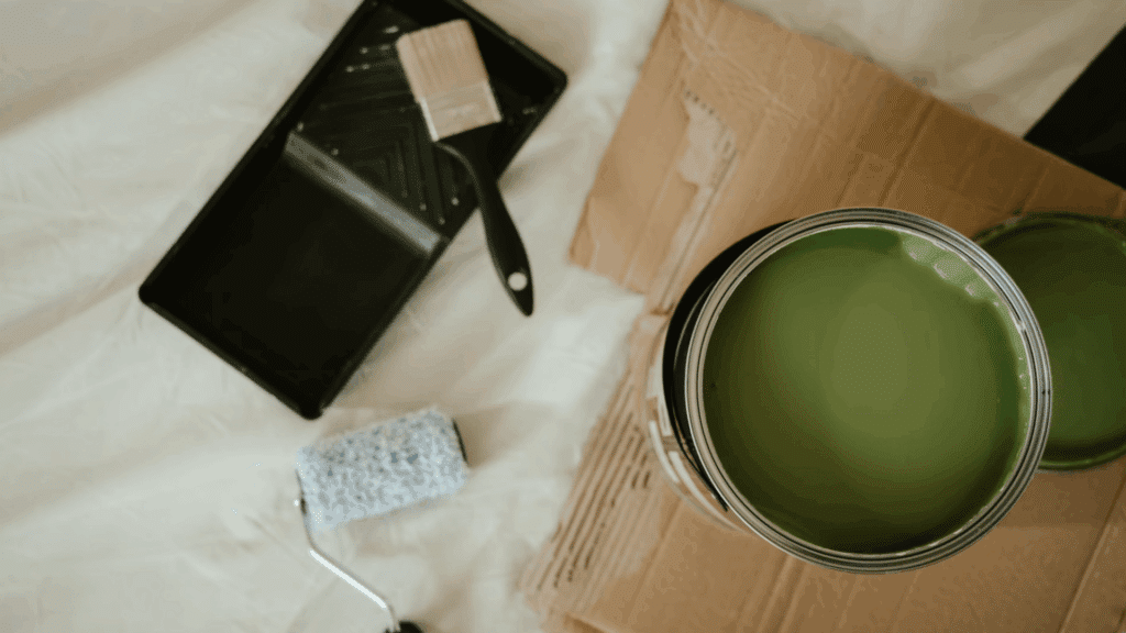 How to Open a Paint Can Safely without Any Mess? open paint can with green paint beside a roller tray brush roller and cardboard on a drop cloth