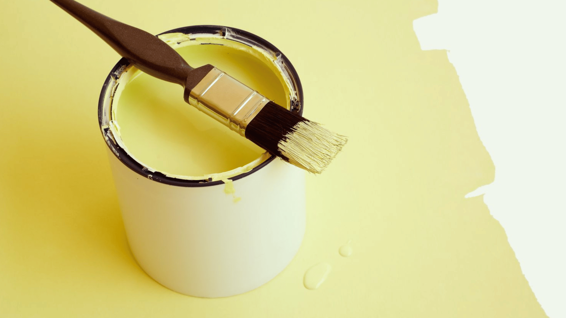 paint brush resting across an open can of yellow paint on a freshly painted yellow surface