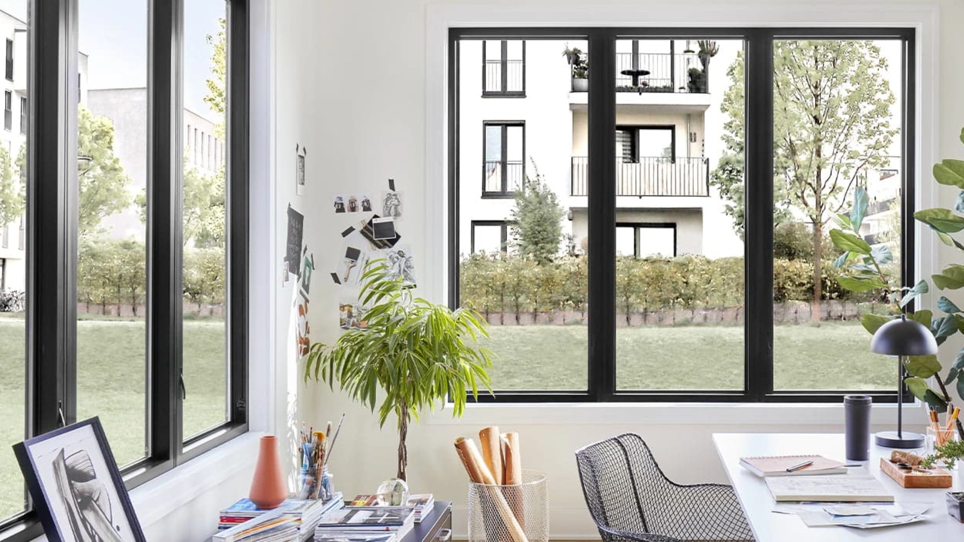 Sleek black fiberglass frame windows in a sunlit modern home office overlooking a lawn.