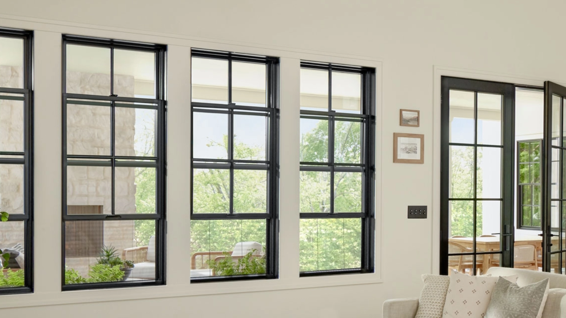 Row of black double-hung windows with grilles in a bright living room interior.