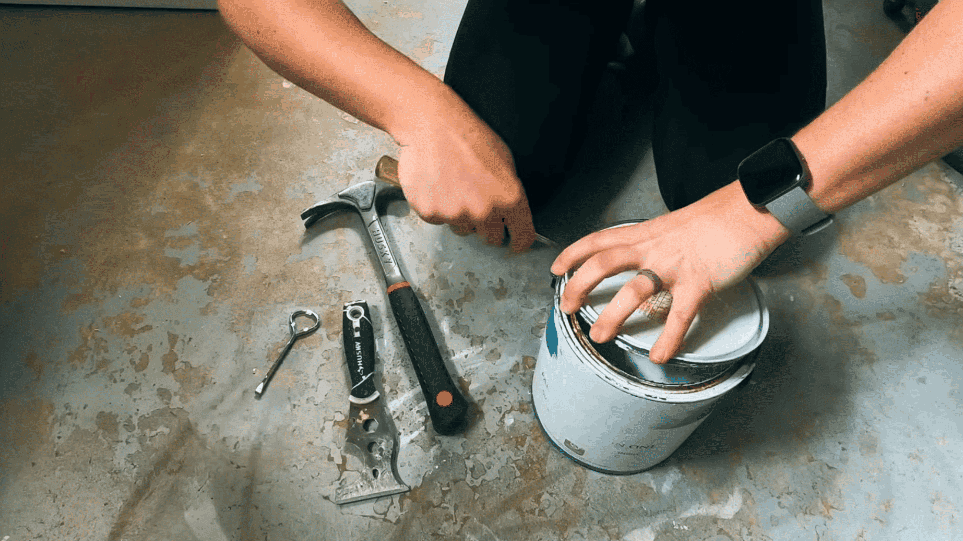 person lifting the loosened lid from a paint can after prying it open with a screwdriver