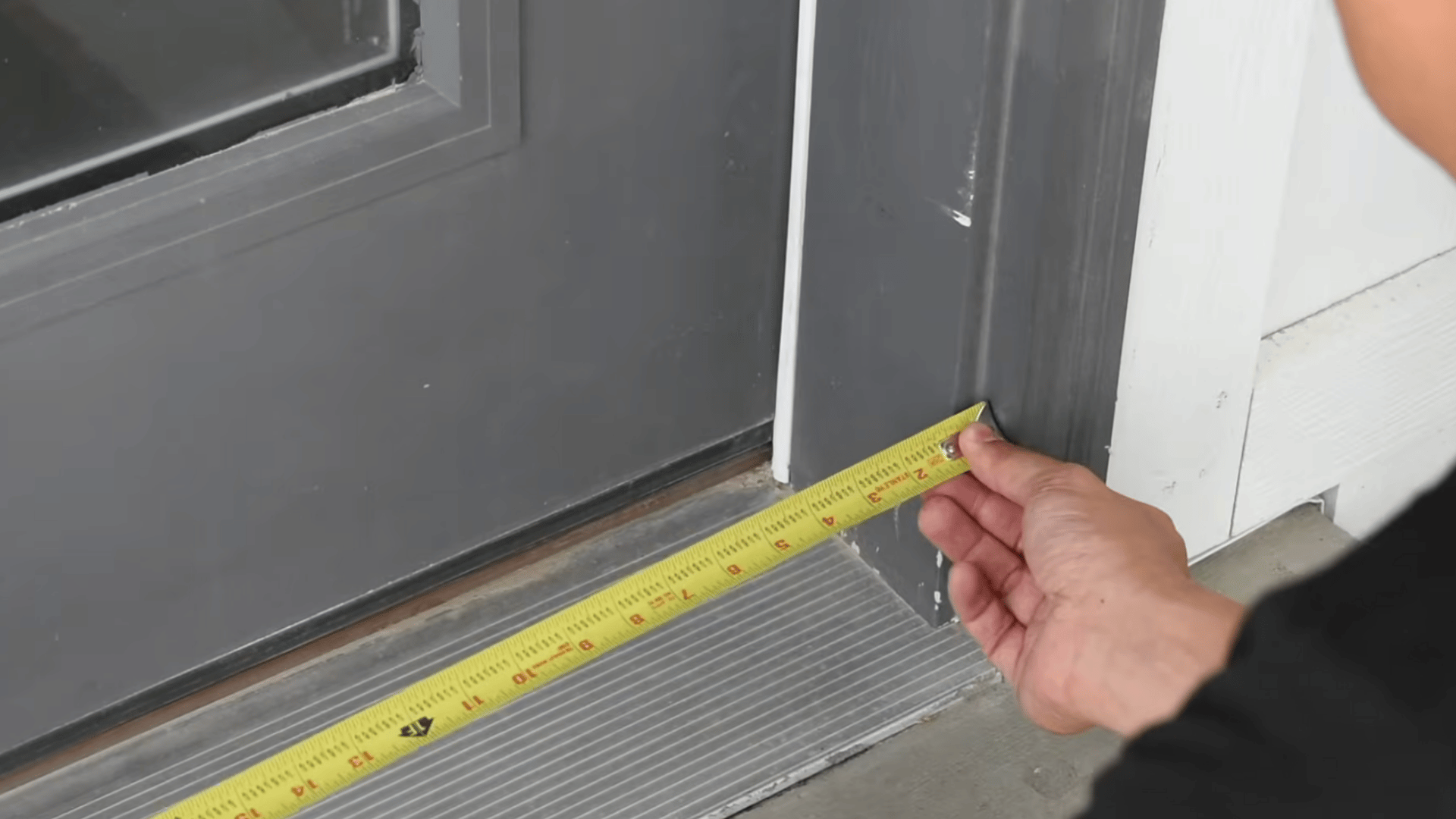 person measuring the width of a doorway threshold with a yellow tape measure to check the door frame opening size
