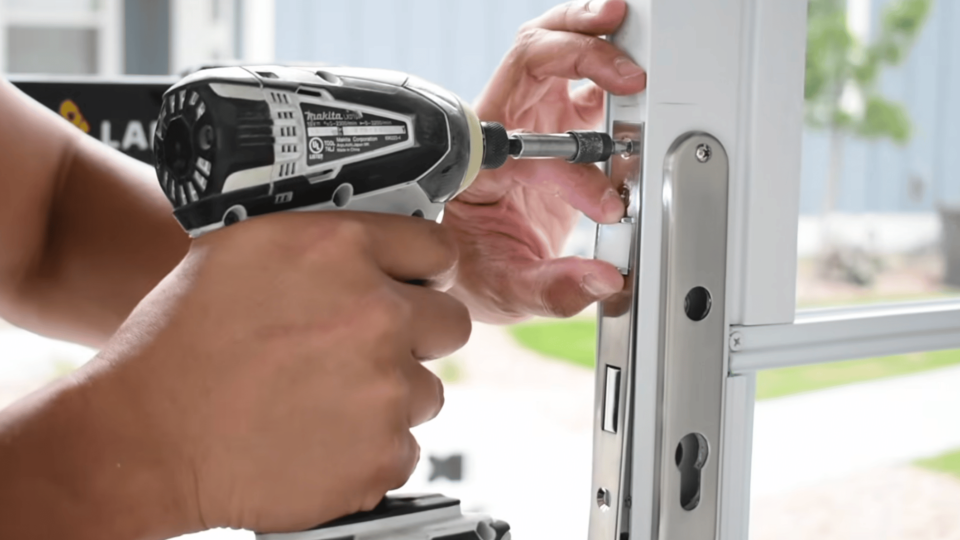 person using a cordless drill to fasten the latch hardware onto a white storm door frame during the installation process