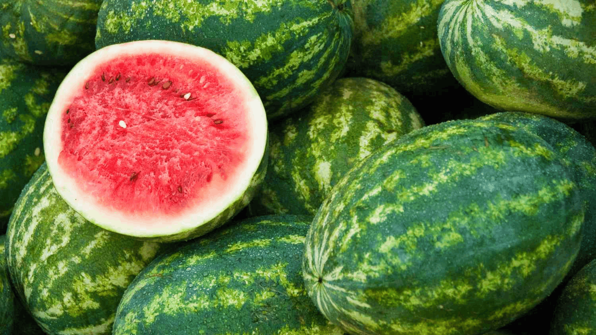 whole watermelons with green striped rinds surrounding a cut watermelon showing bright red flesh and black seeds ready to eat
