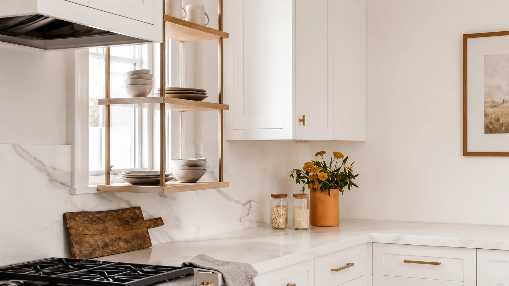 Minimalist white kitchen with open wooden shelving, ceramic dishes, marble countertop, brass accents, and warm natural light.