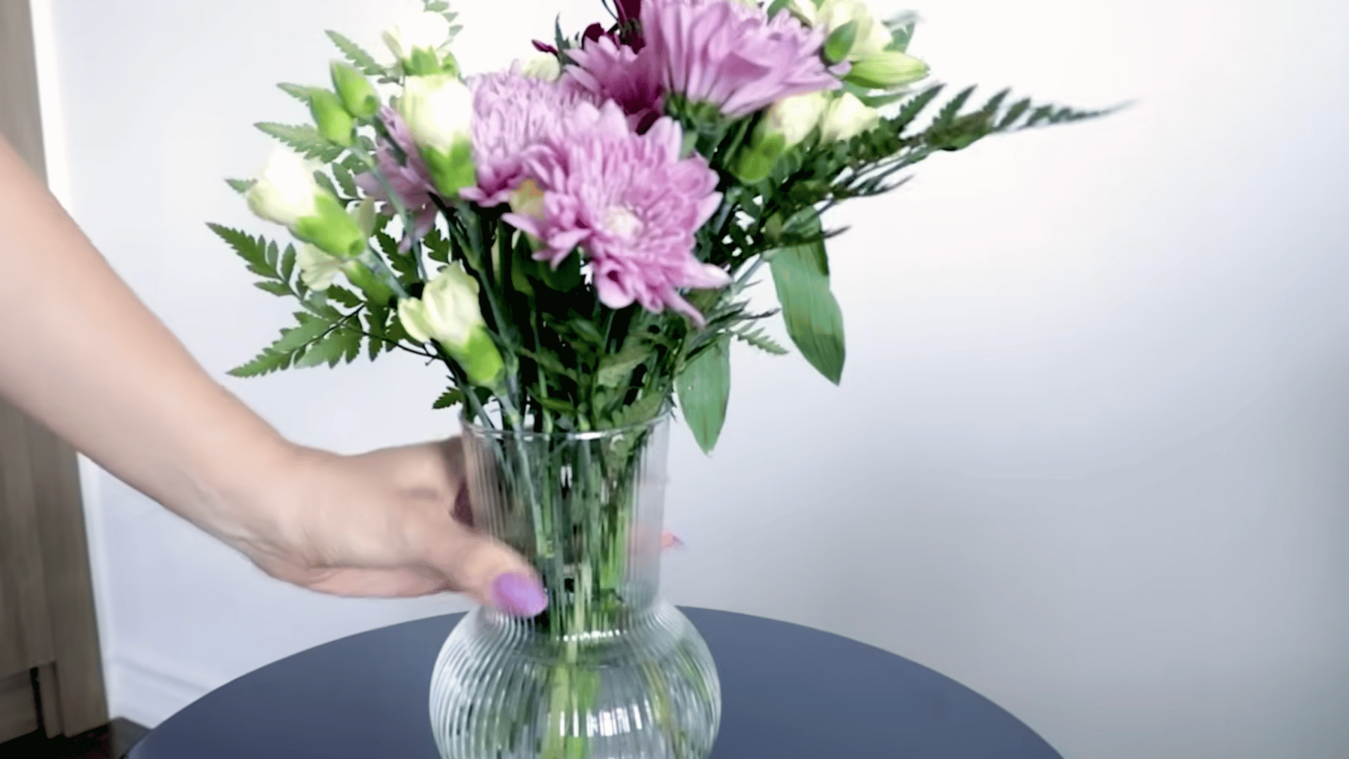 a person places a freshly arranged bouquet into a clear ribbed glass vase creating a balanced floral display on a table