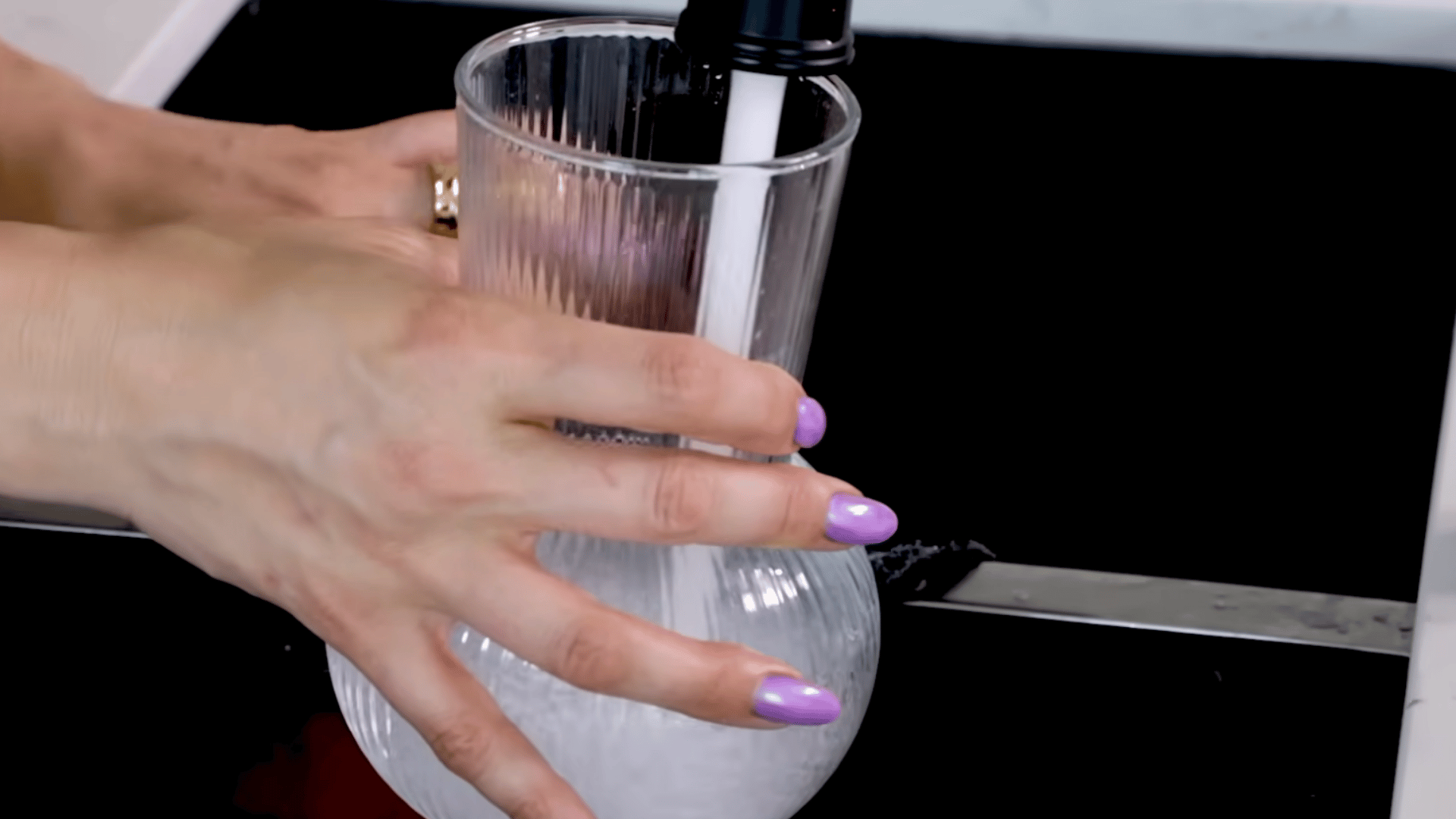 a person rinses a clear glass vase under running water in a kitchen sink to prepare it for arranging fresh flowers