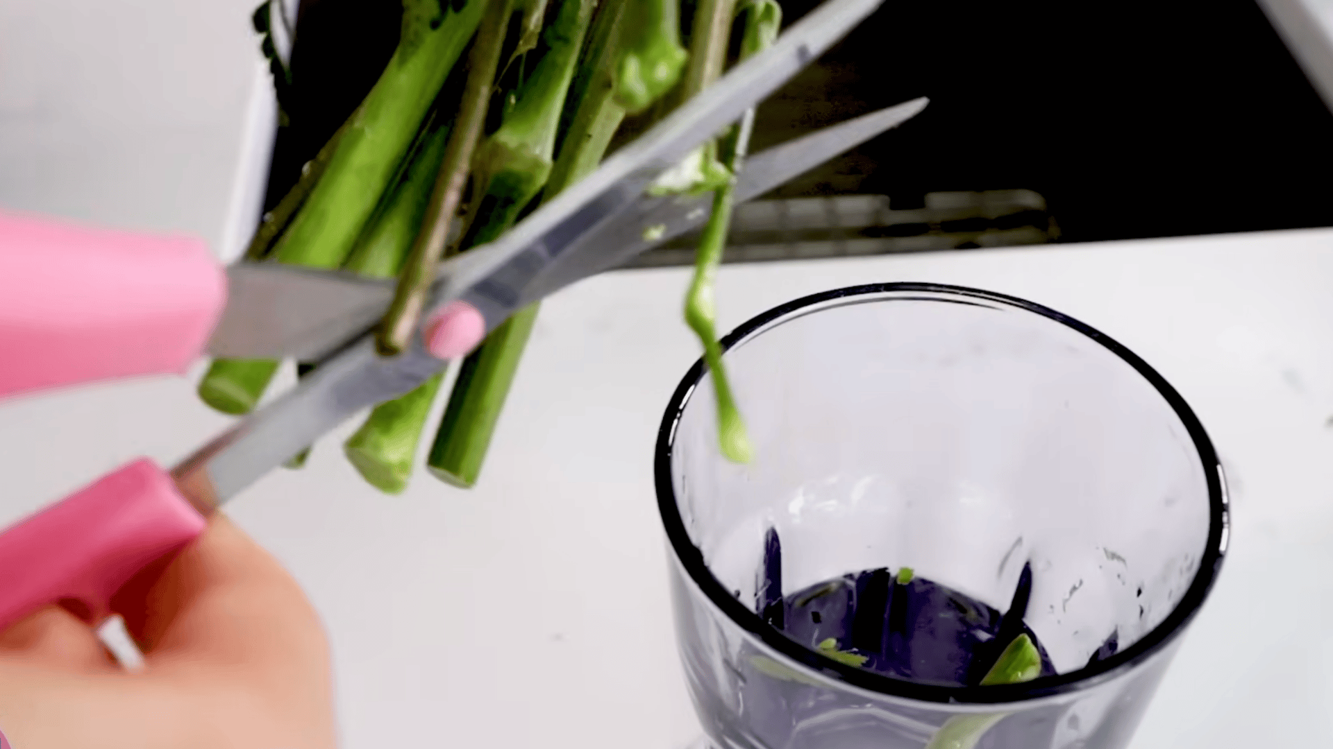 a person trims flower stems with pink handled scissors over a container before placing the fresh bouquet into a clean vase