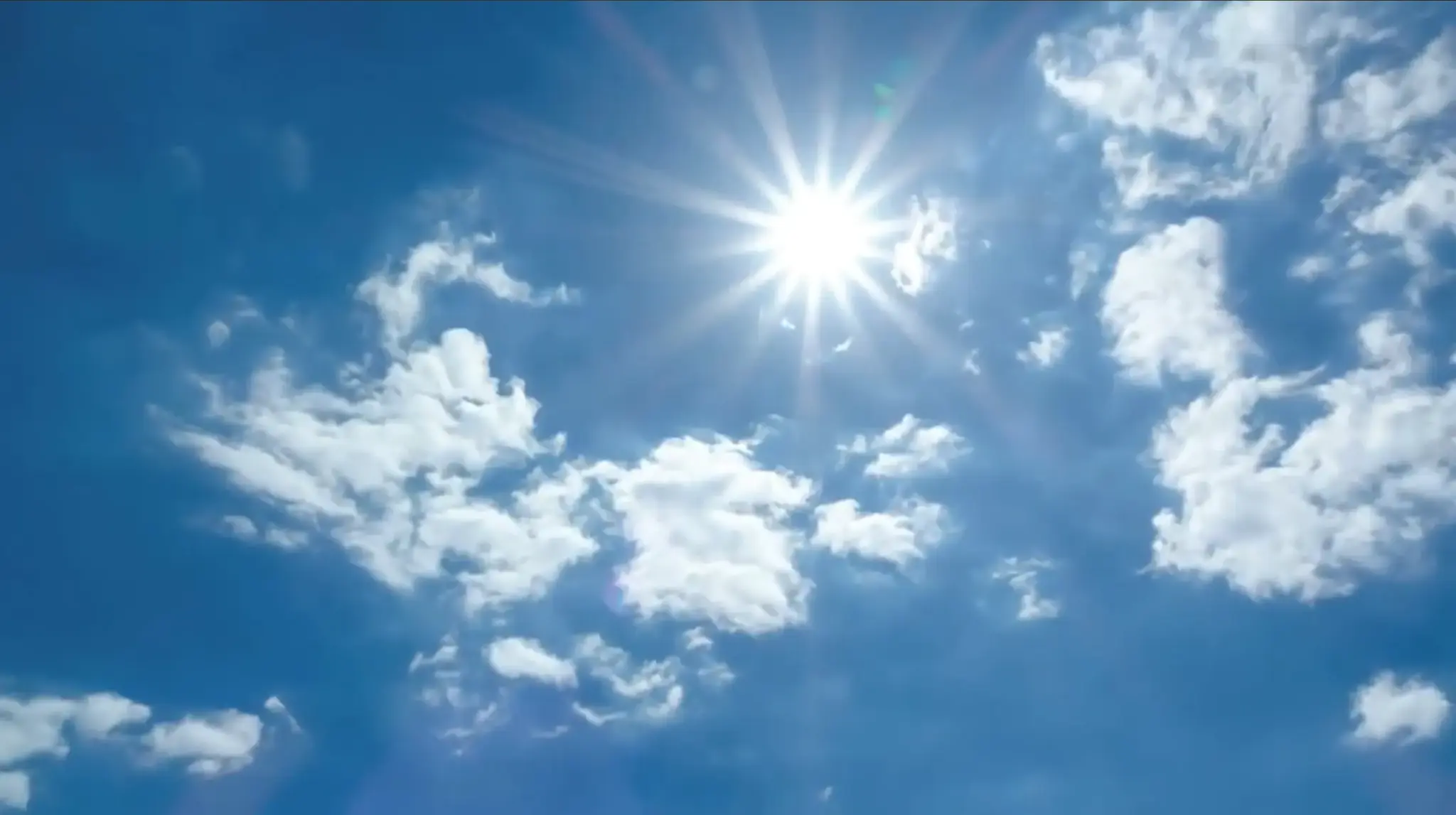 Bright sun shining through scattered white clouds in a clear blue sky.