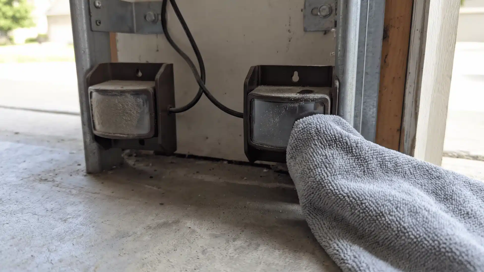 Two garage door sensors near the floor with a soft cloth wiping dust from one lens