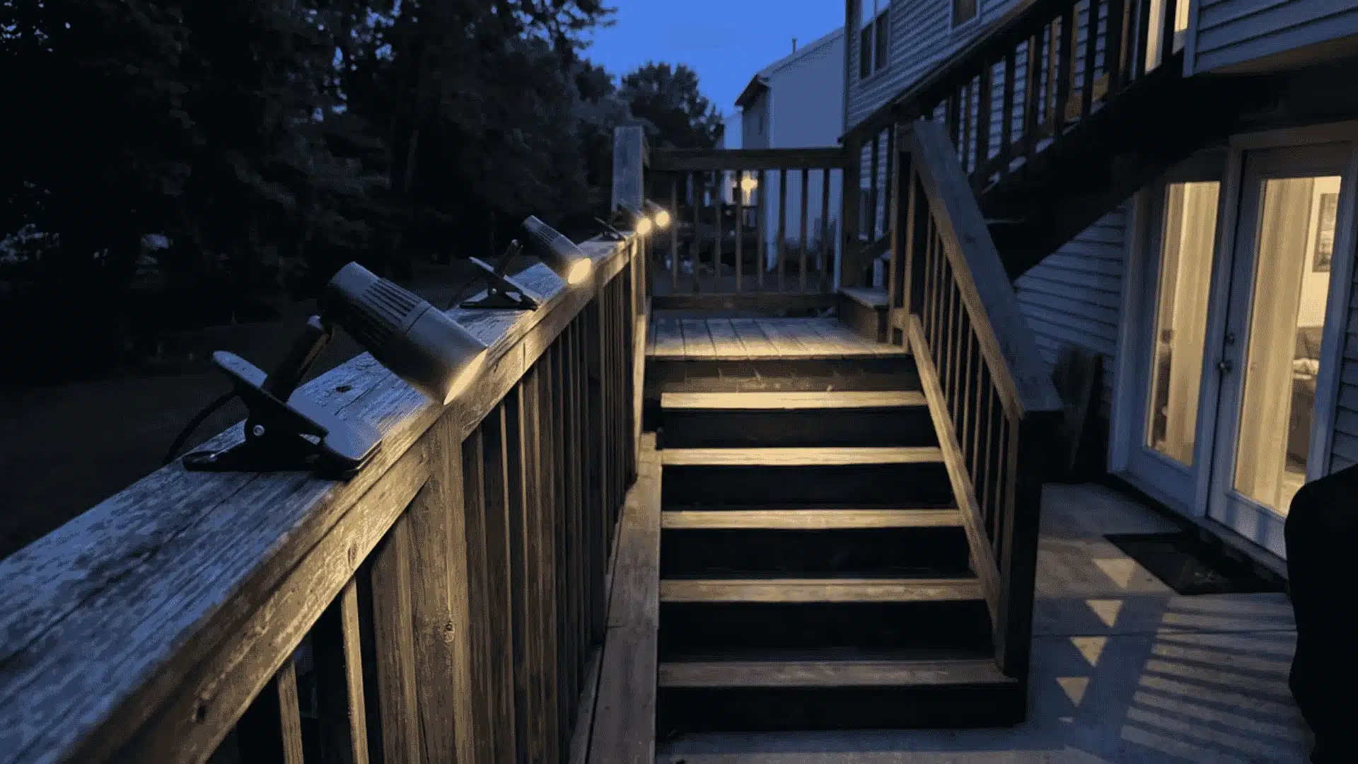 Clip-on spotlights attached to a deck railing and aimed at wooden stairs