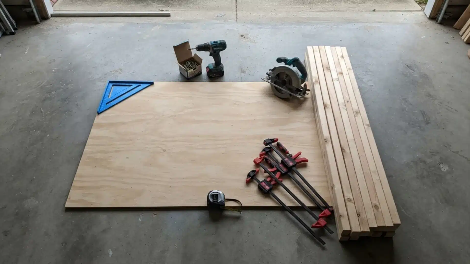 Plywood, wooden studs, circular saw, drill, clamps, and measuring tools laid out on garage floor.