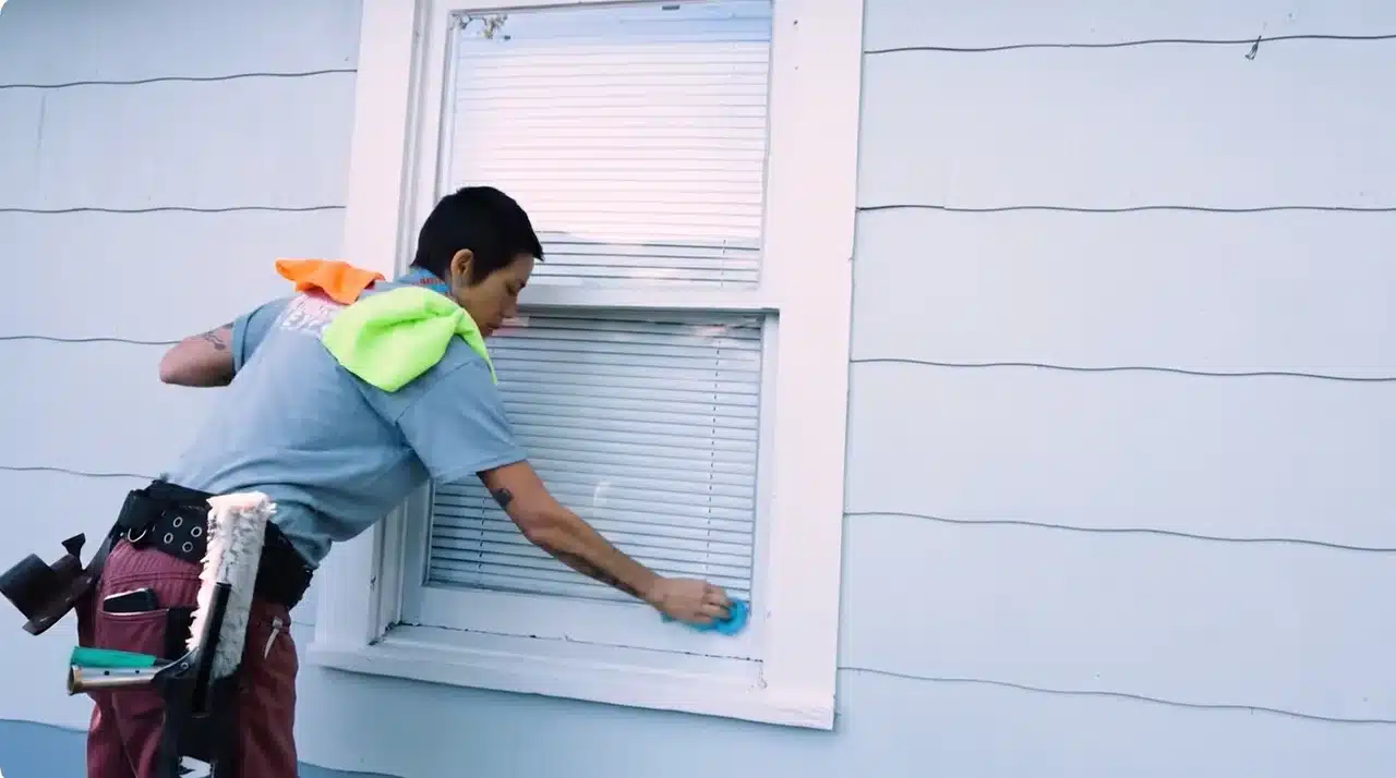 Window cleaner drying the bottom frame and sill with a blue microfiber cloth.