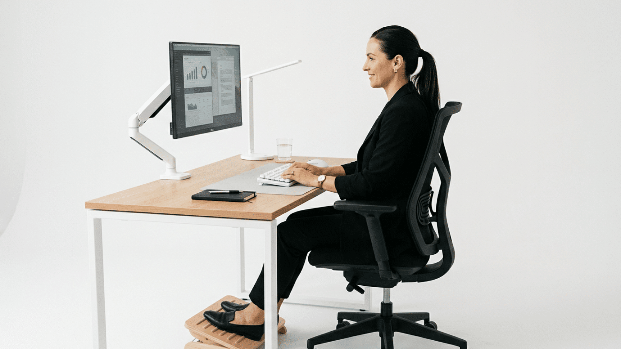 person sitting with proper posture in an ergonomic office chair at a desk using monitor keyboard and footrest