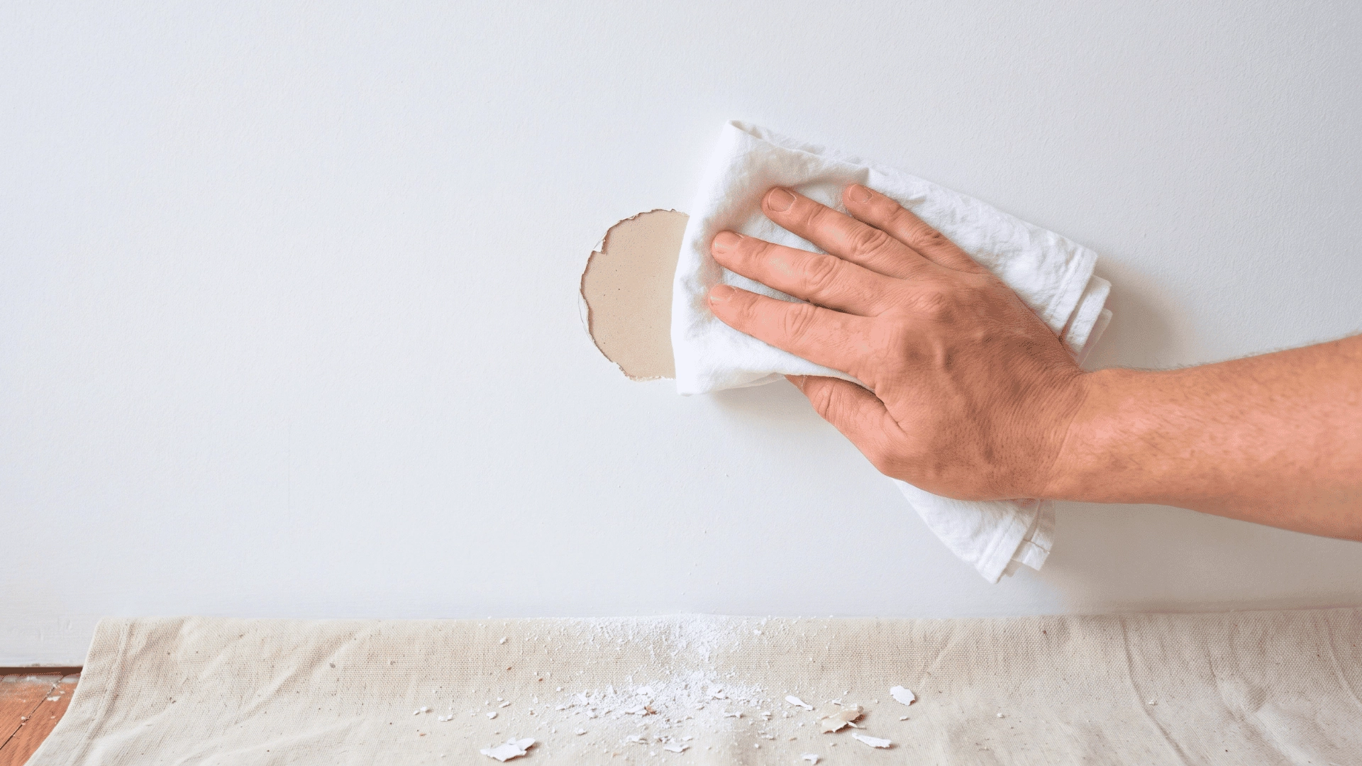 Hand cleaning a damaged white wall with a cloth after removing peeling paint chips.