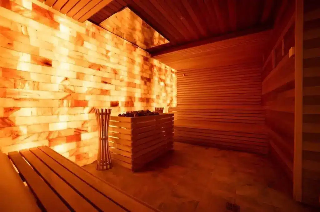 Warmly lit sauna interior with wooden benches and a salt wall feature