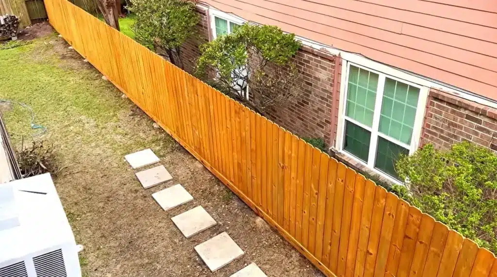 How to Build a Fence Step by Step DIY Guide Aerial view of a newly stained wooden fence surrounding a backyard with a stepping stone walkway.