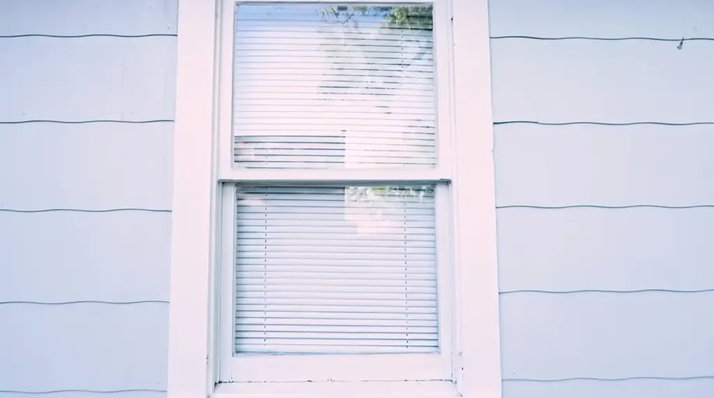 How to Clean Windows Without Streaks Clean double-pane window with white trim on the exterior wall of a house.