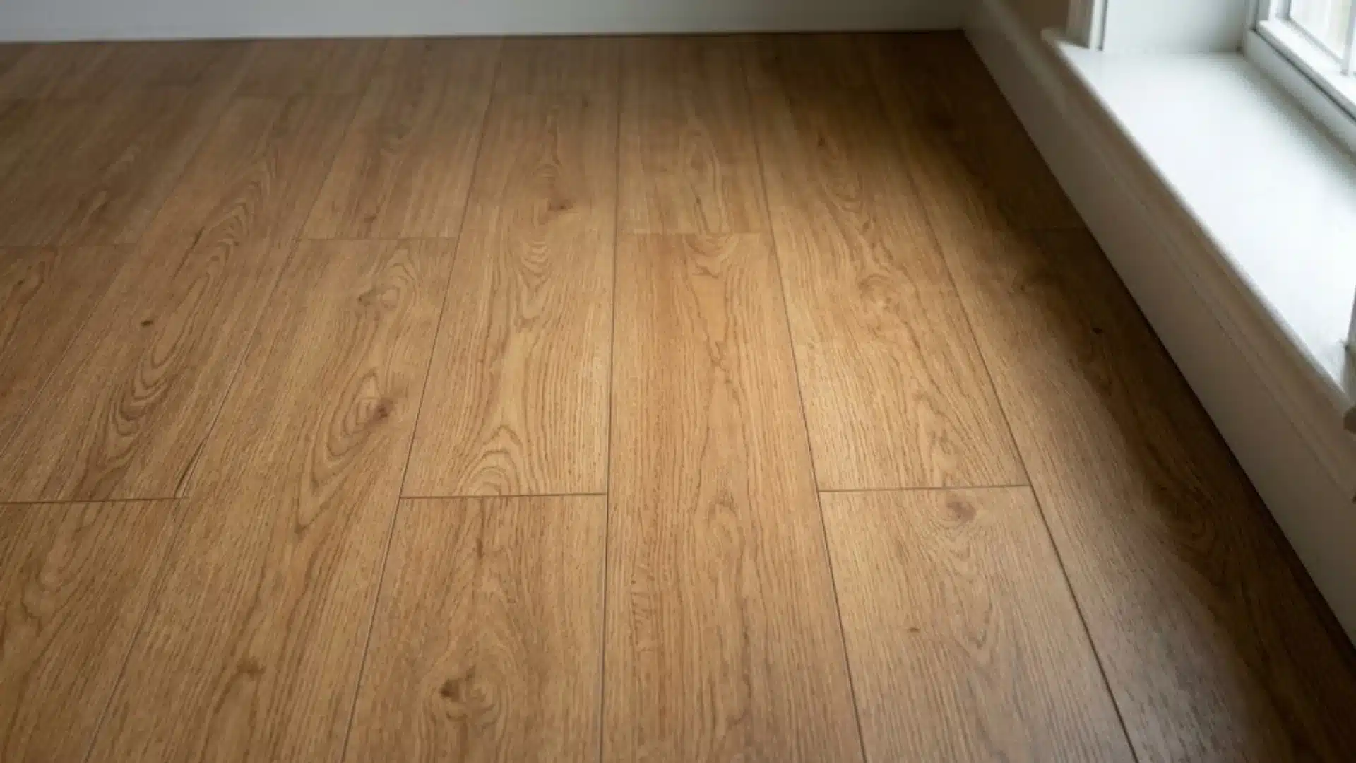 laminate wood look flooring planks installed in a small bedroom near a window sill