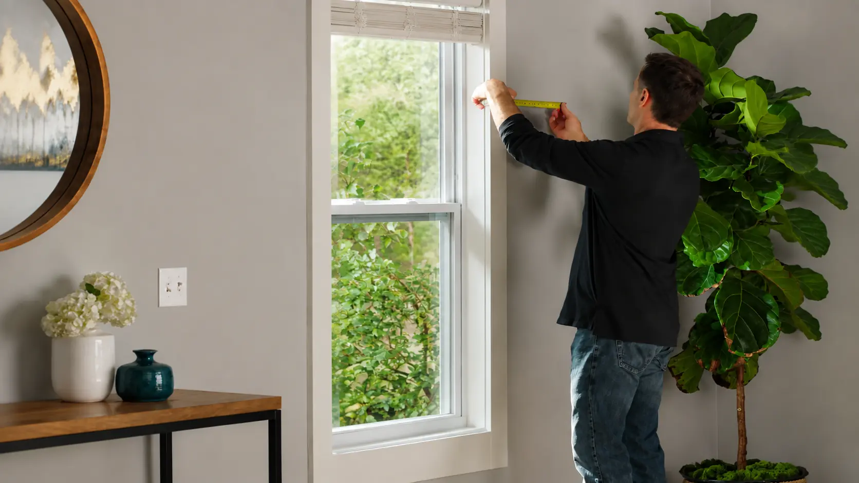 Person measuring a window with a tape measure before installing curtain treatments