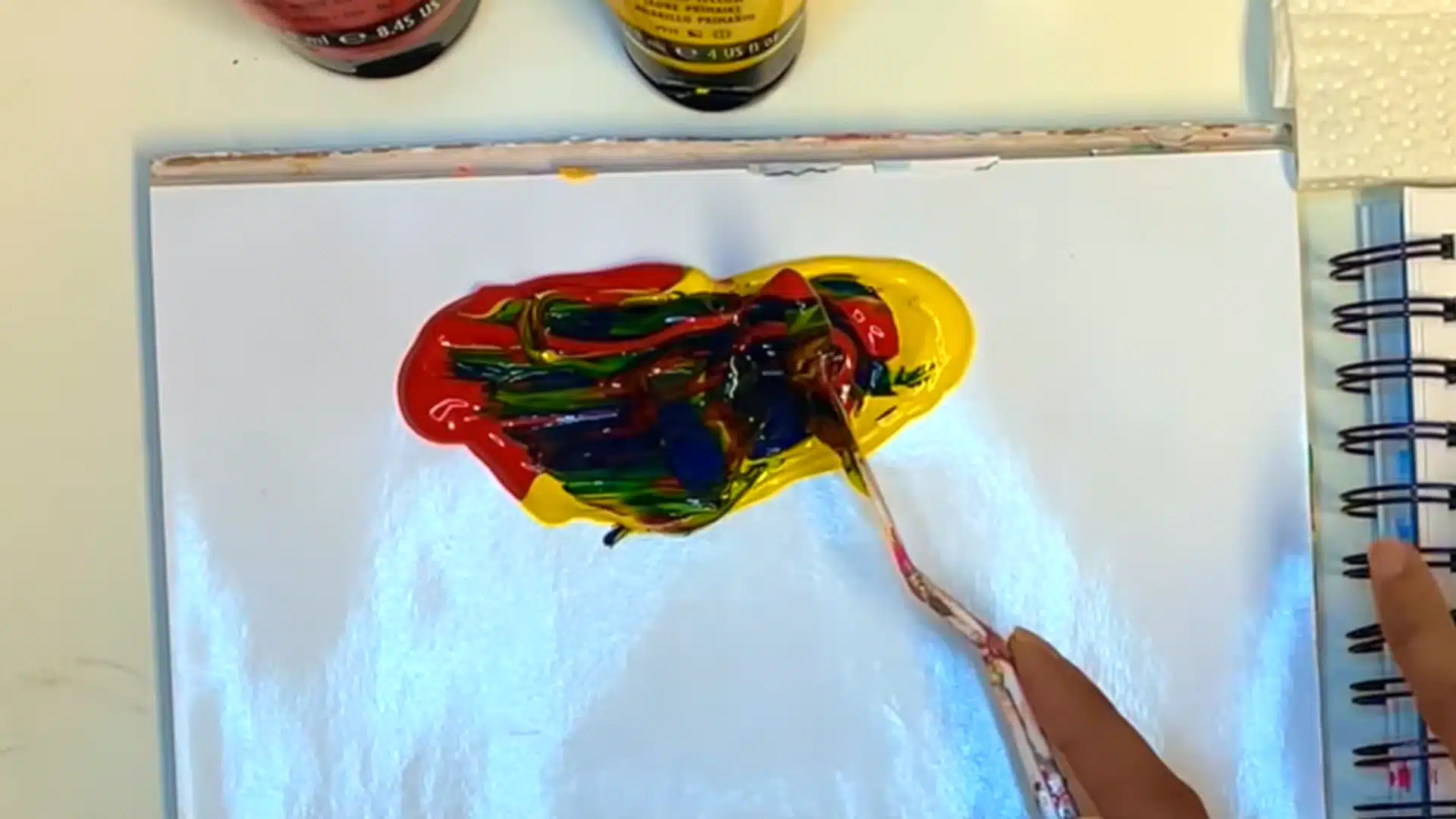 Mixing equal parts of red, yellow, and blue paint to create a basic brown color on a palette.