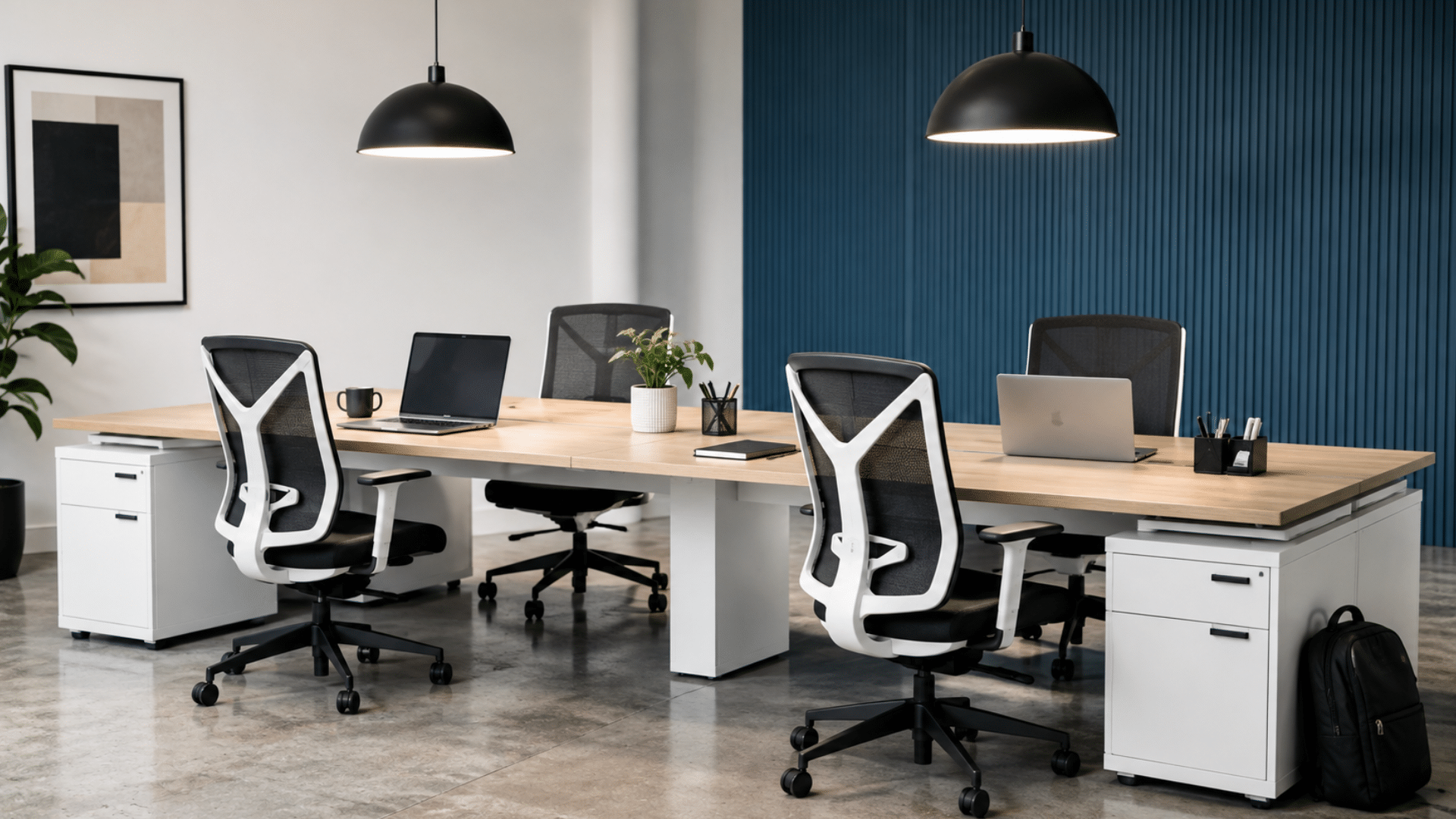minimalist office with a long light wood desk, four black and white ergonomic mesh chairs laptops and pendant lights