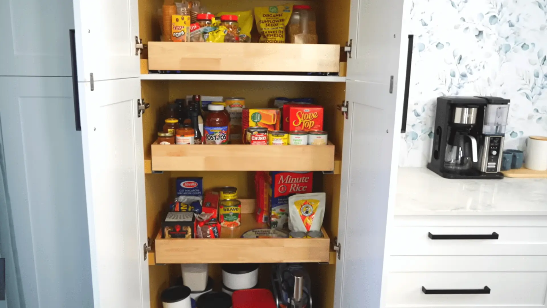 Organized pantry cabinet with pull-out shelves grouping snacks, canned goods, pasta, rice, and other foods.