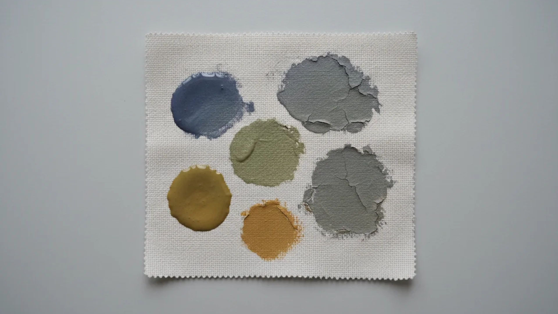 A white fabric square displaying various dried and cracked color paint swatches.