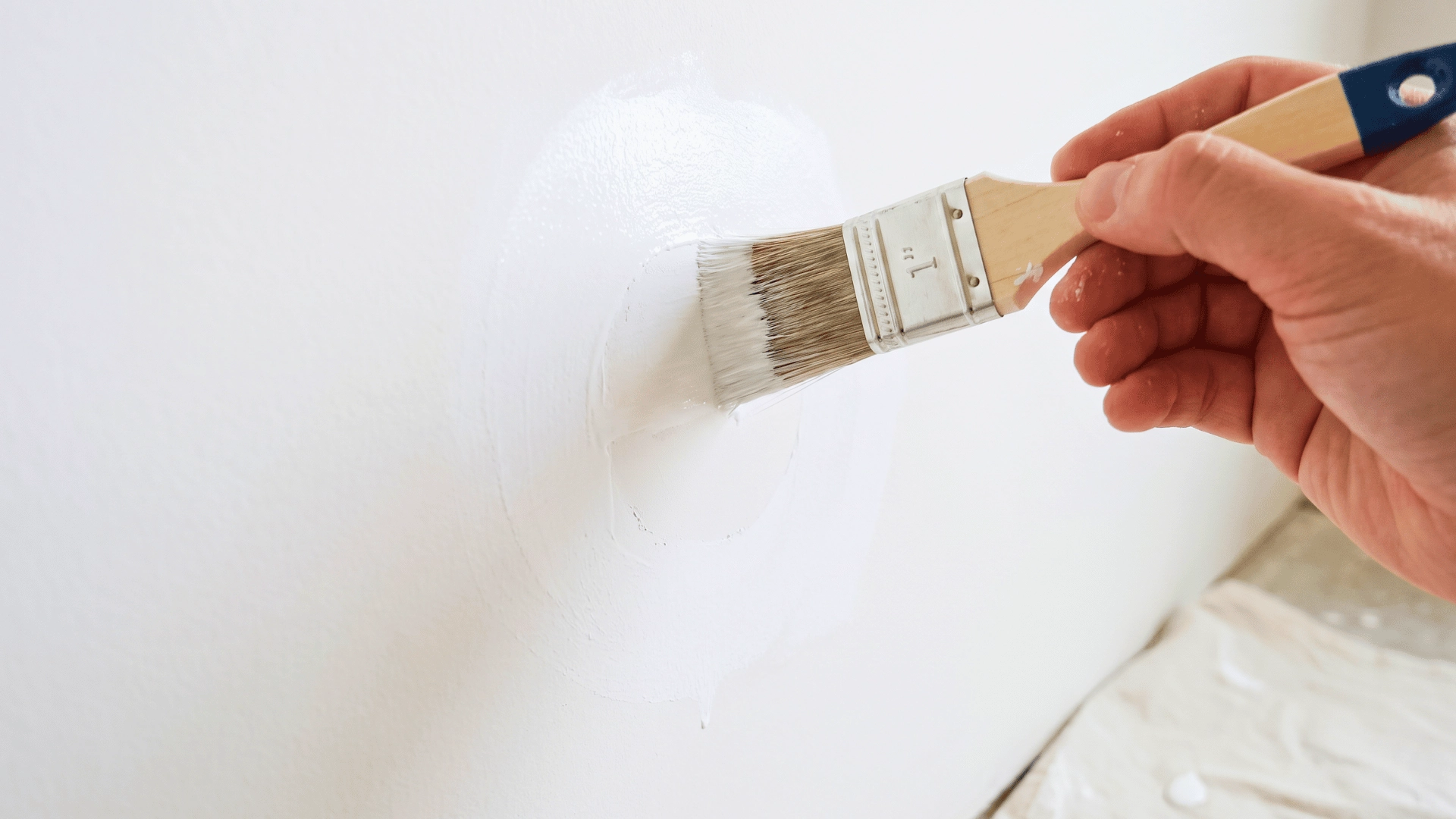 Paintbrush applying primer over a patched wall area during a paint repair project.